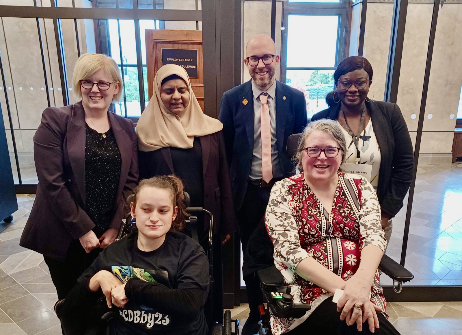 A group of people six people, including Minister Carla Qualtrough and Green MP Mike Morrice stand with representatives from Disability Without Poverty