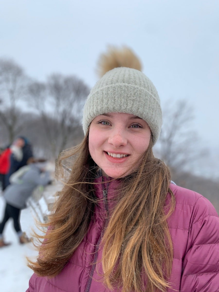 Breanna MacLeod, 21, smiles at the camera. She has long, light brown hair and wears a burgundy coat and beige toque with a pompom.