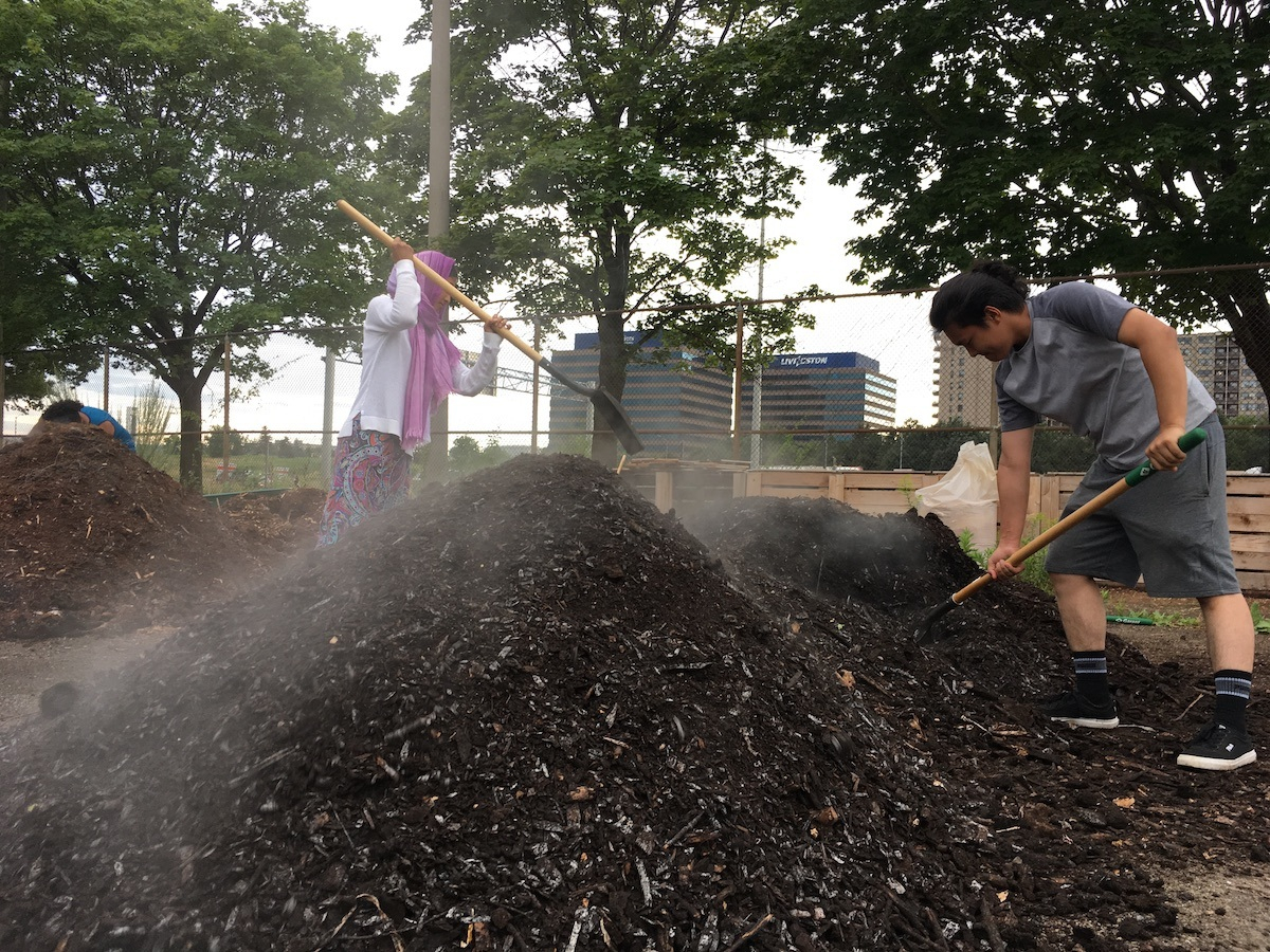 Two people shovelling a pile of soil
