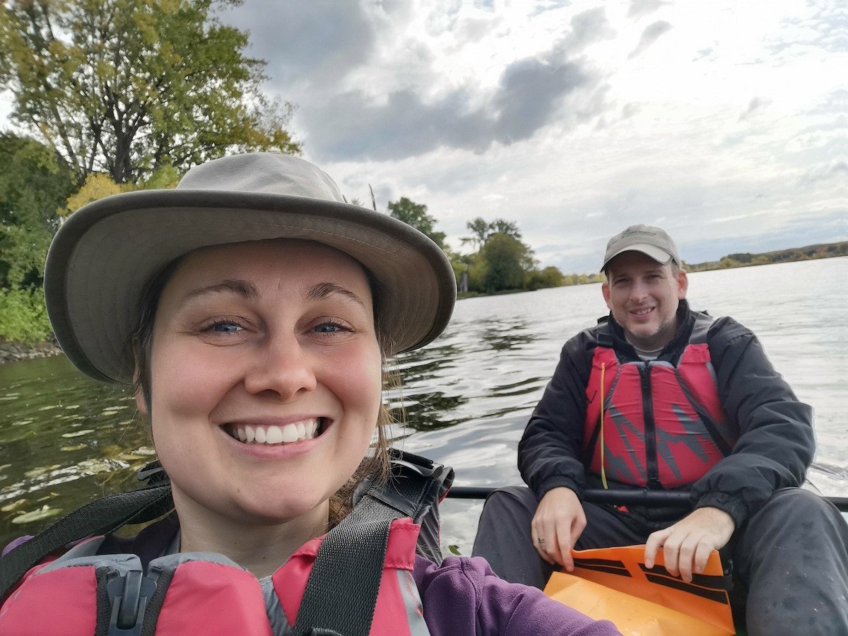 A woman and man smile at the camera while sitting in a kayak on a lake