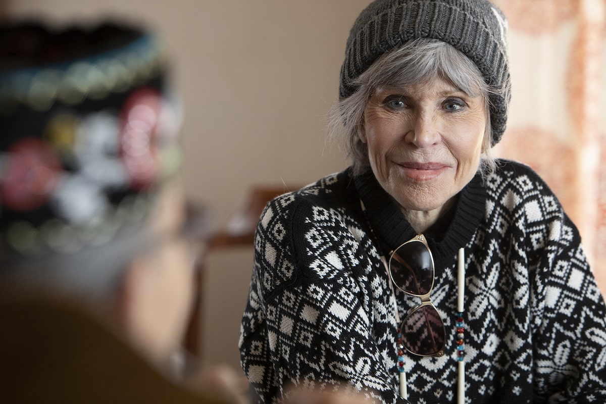 A grey-haired woman in a toque and a sweater looks past the camera