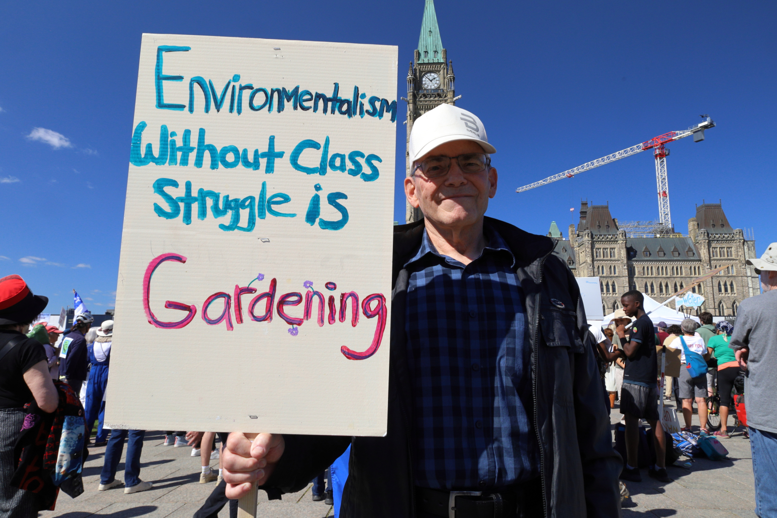 A man holds a sign that says 'environmentalism without class struggle is just gardening'