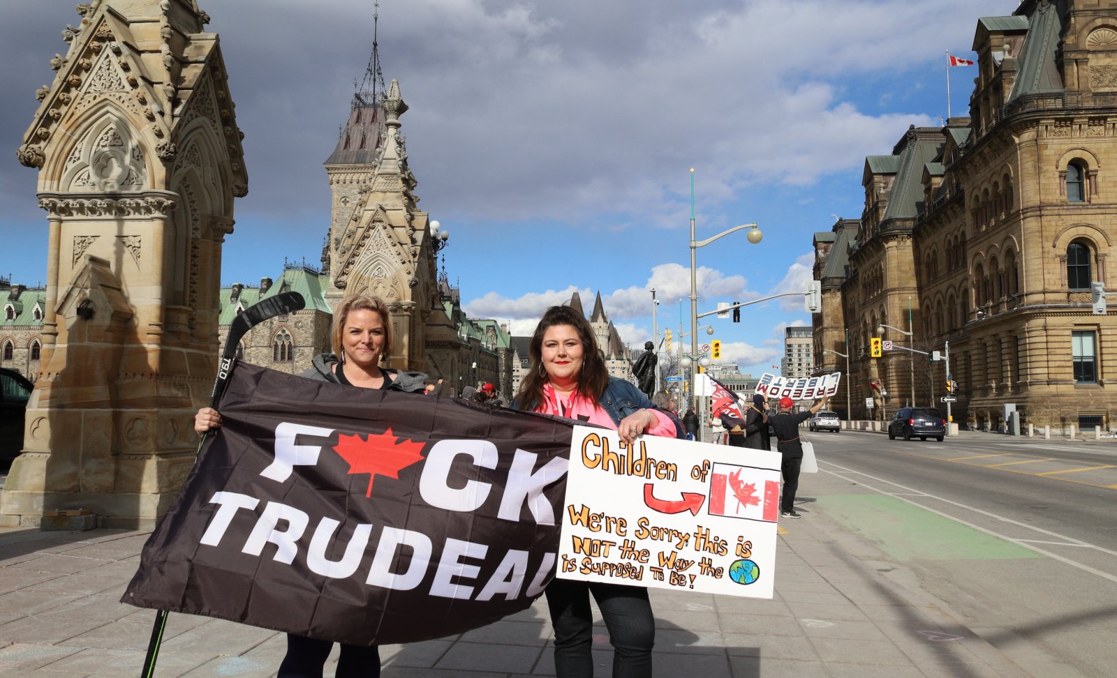 Two women stand together holding signs and a flag at a protest in Ottawa on April 1 2024
