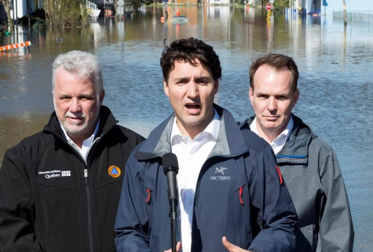 Quebec Premier Philippe Couillard and Gatineau MP Steve McKinnon look on as Canadian Prime Minister Justin Trudeau speaks to media following a tour of a flooded area of Gatineau, Que. Thursday May 11, 2017. Photo by the Canadian Press/Adrian Wyld