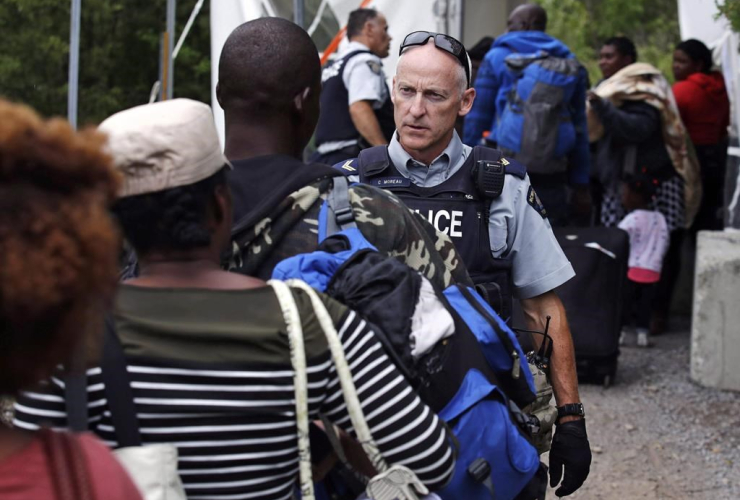 An RCMP officer standing in Saint-Bernard-de-Lacolle, Que., advises migrants that they are about to illegally cross from Champlain, N.Y., and will be arrested, Monday, Aug. 7, 2017. Canadian Press/AP