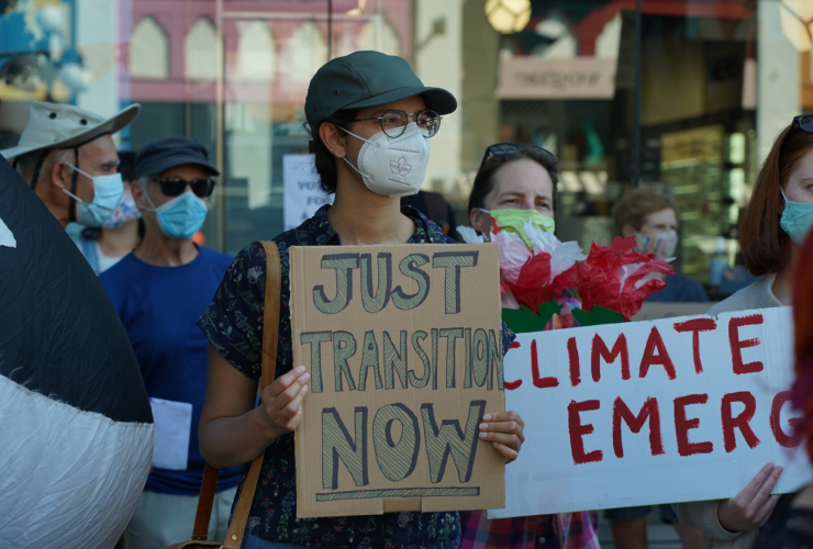 A woman holds up a "Just Transition Now" sign amidst other people protesting for climate action.