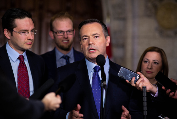 Alberta's premier Jason Kenney answers questions while reporters hold recording devices and microphones up to him.