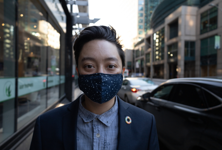 A person stands in the street in downtown Ottawa, wearing a dark blue mask