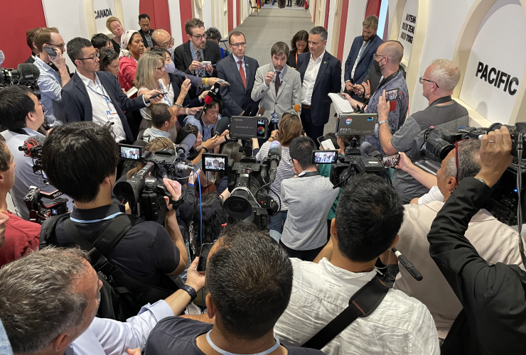 A man is surrounded by a large group of reporters with cameras and microphones