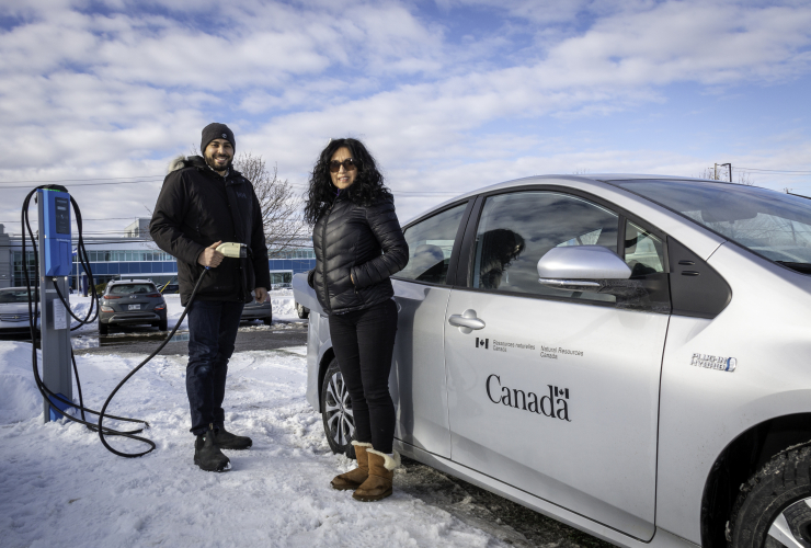 two people stand beside an electric vehicle in the winter