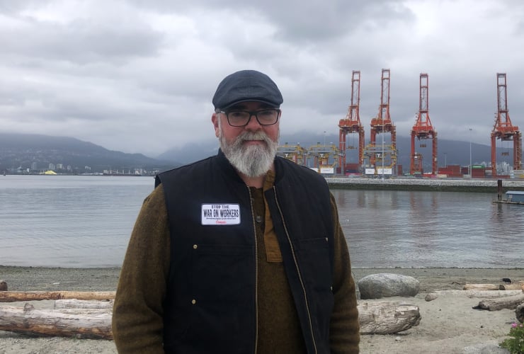 A bearded man stands in front of a small shipping terminal in Vancouver