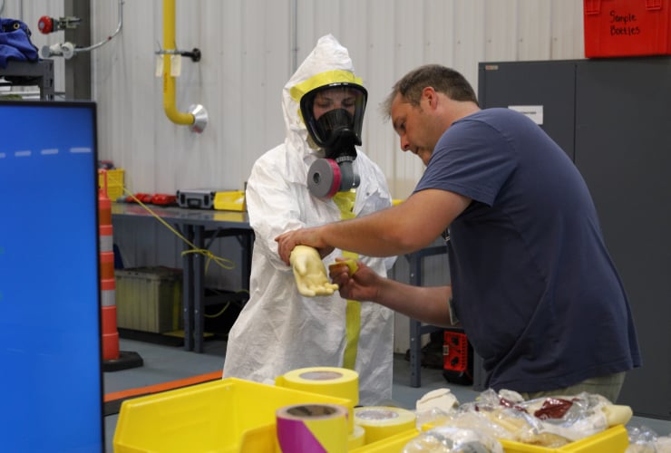A person putting on a hazmat suit, taping it all up so there's no gaps, with the help of another individual